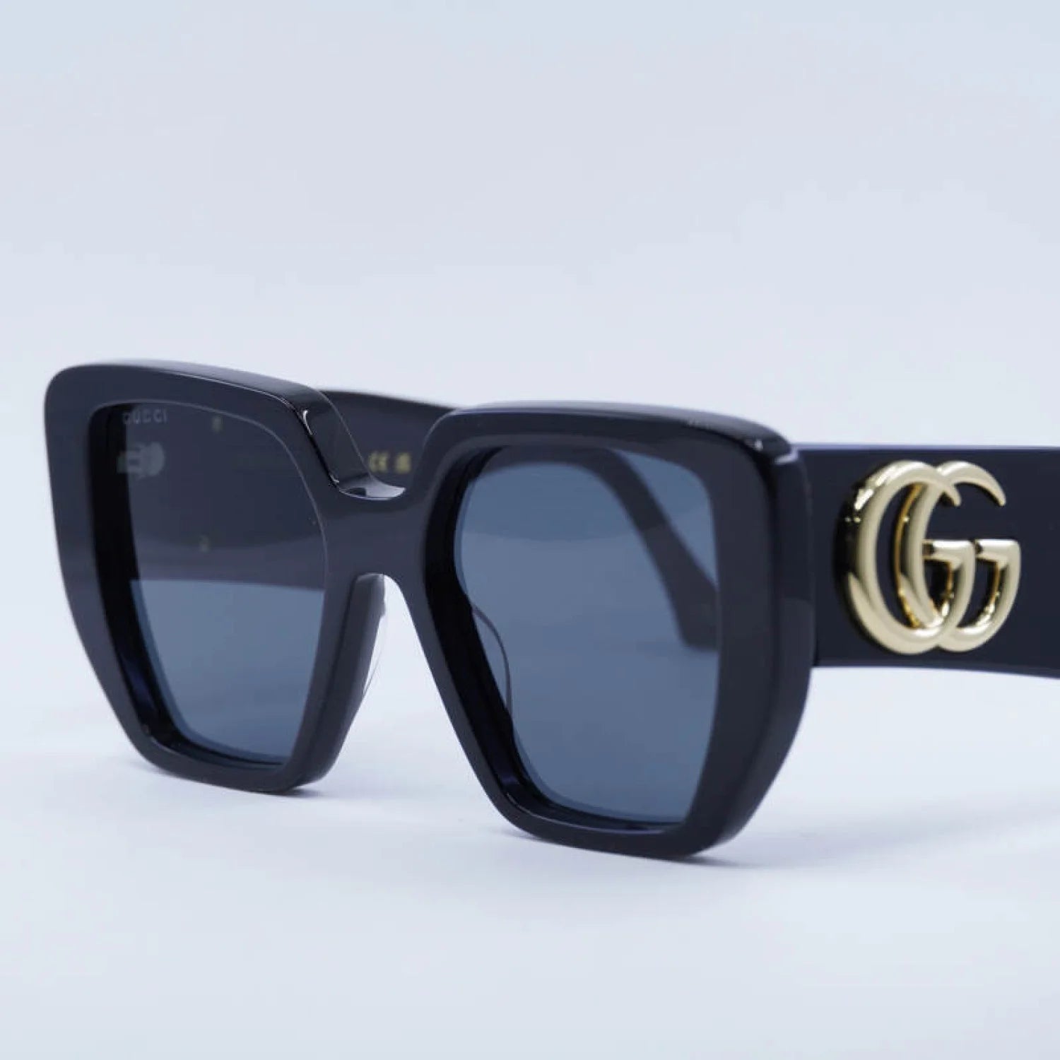 Black sunglasses with a gold 'GG' logo on a light gray background